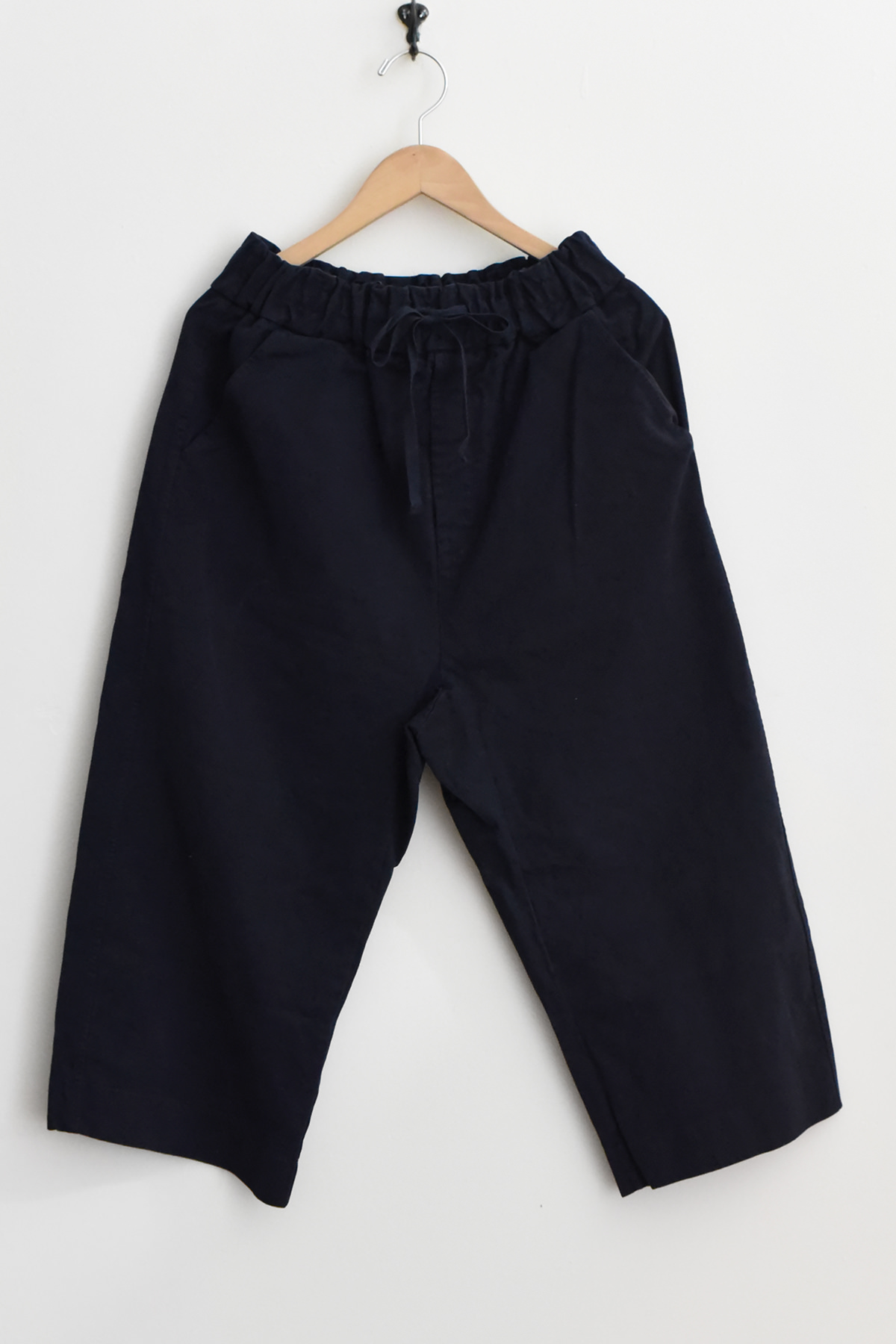 Album di Famiglia 23269 Wide & Short Trousers WCC in navy, featuring a wide-leg silhouette with an elastic waistband and drawstring, displayed on a wooden hanger against a plain white wall.