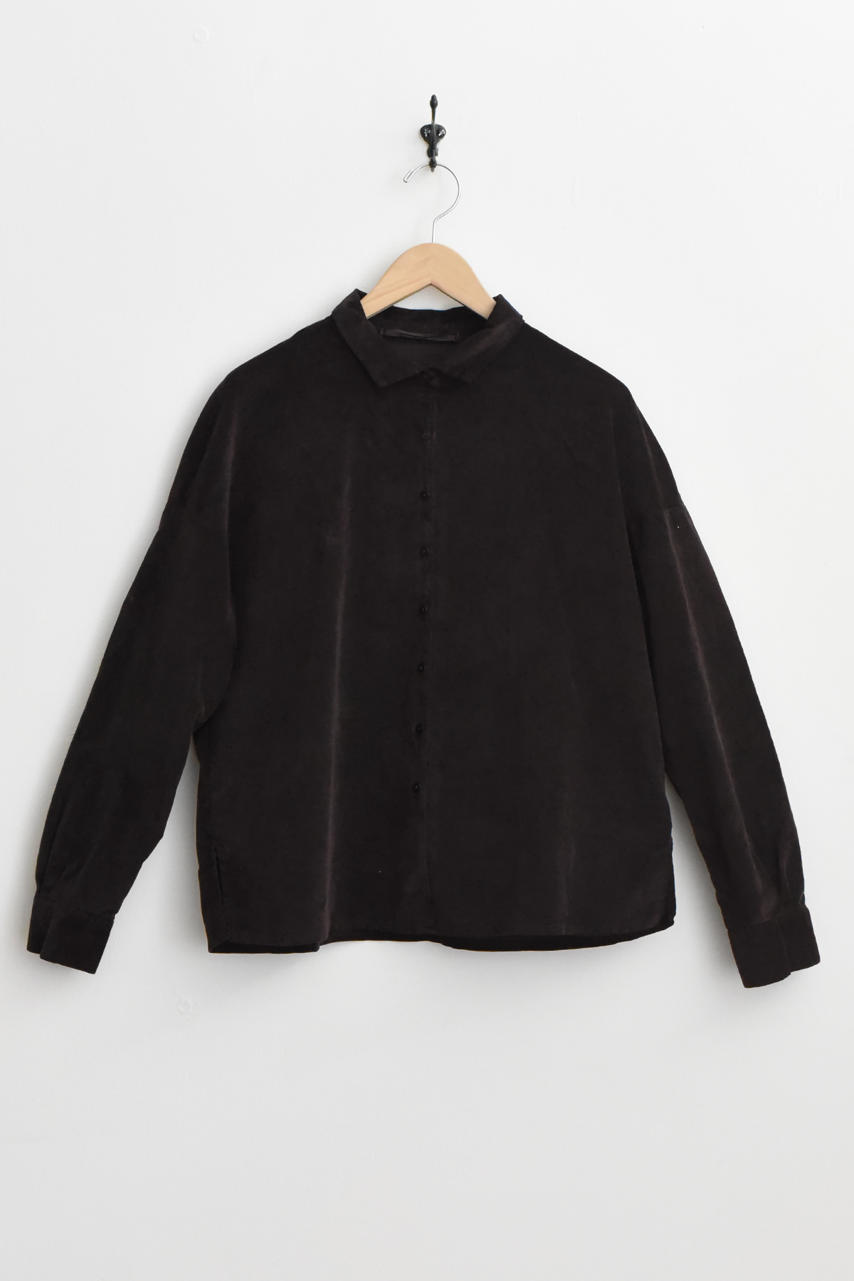 The Album di Famiglia 12170 Short Collar Shirt Velvet in brown, featuring long sleeves and a button-up front with a short collar, hangs on a wooden hanger against a plain white wall. ベルベットシャツ アルバムディファミリア