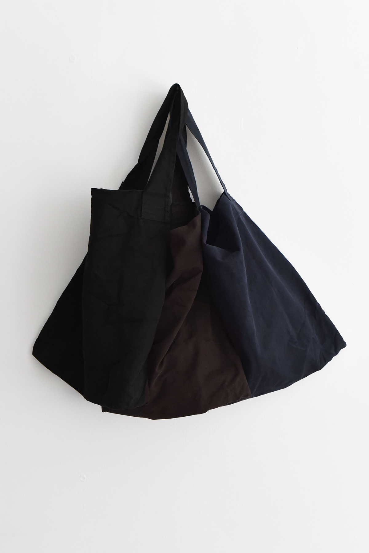 Three large Album di Famiglia 9297 bags in black, navy, and brown hang by their handles on a plain white wall.