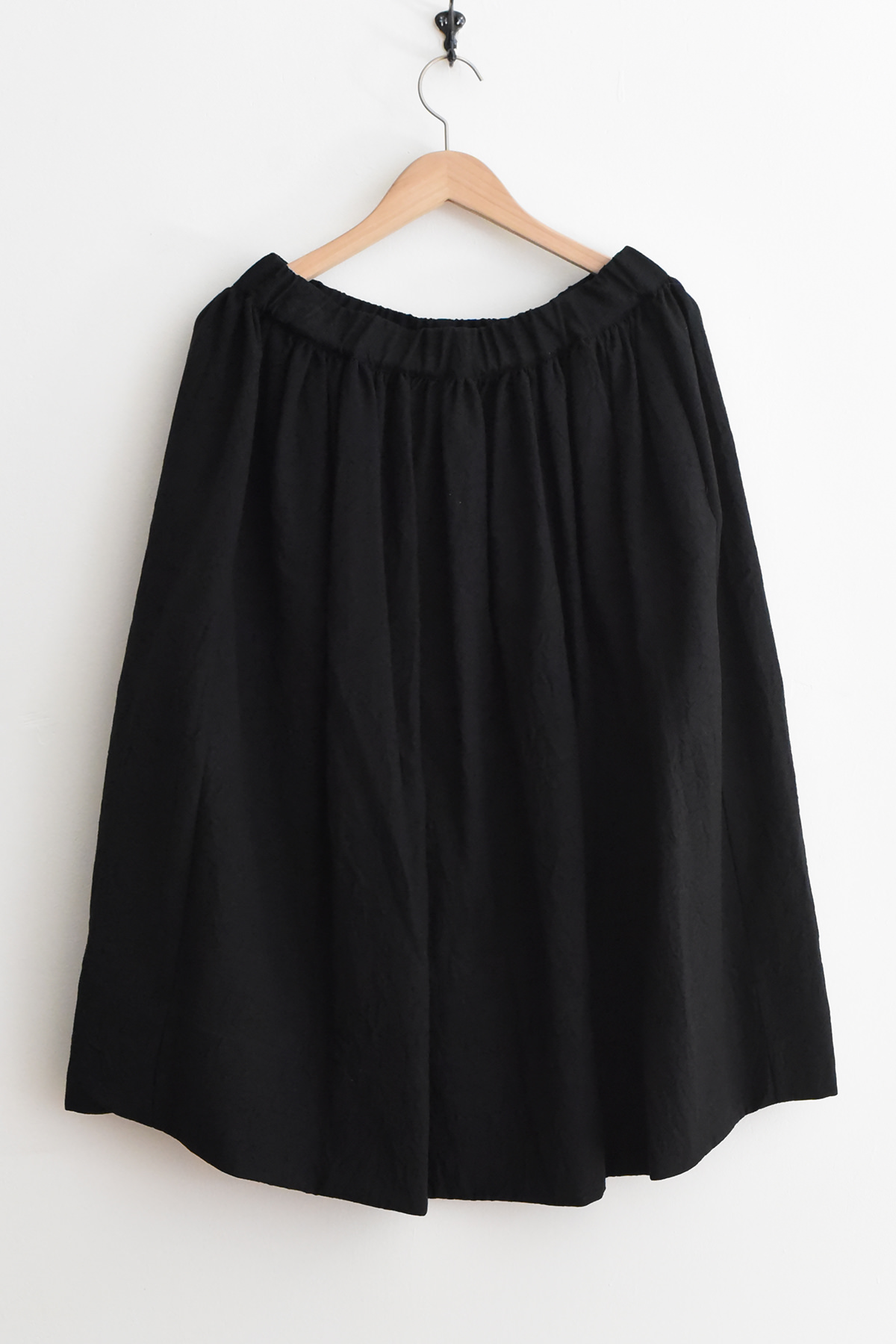 Black apuntob (a.b) P1569 Skirt with a gathered elastic waist hanging on a wooden hanger.